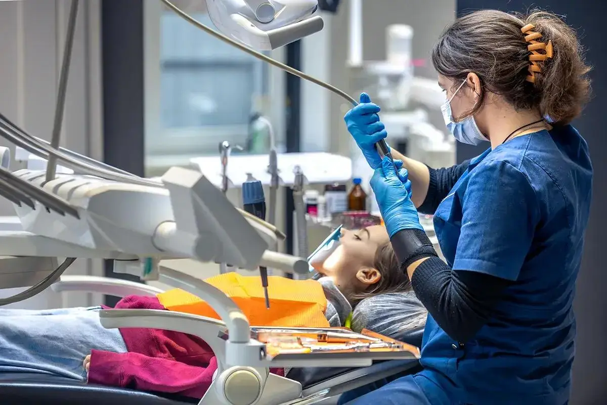 Dental professional treats patient in modern clinical treatment room setting.