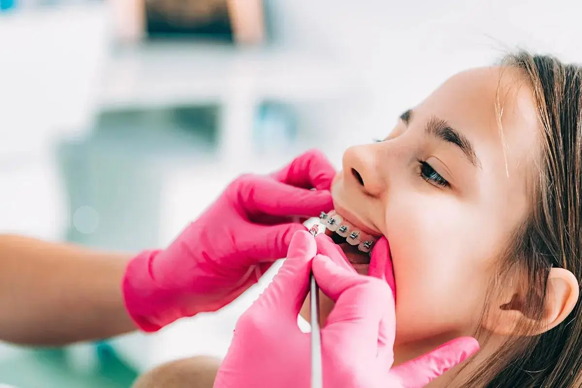 A dental professional in pink gloves adjusting a patient's braces during a routine orthodontic procedure.