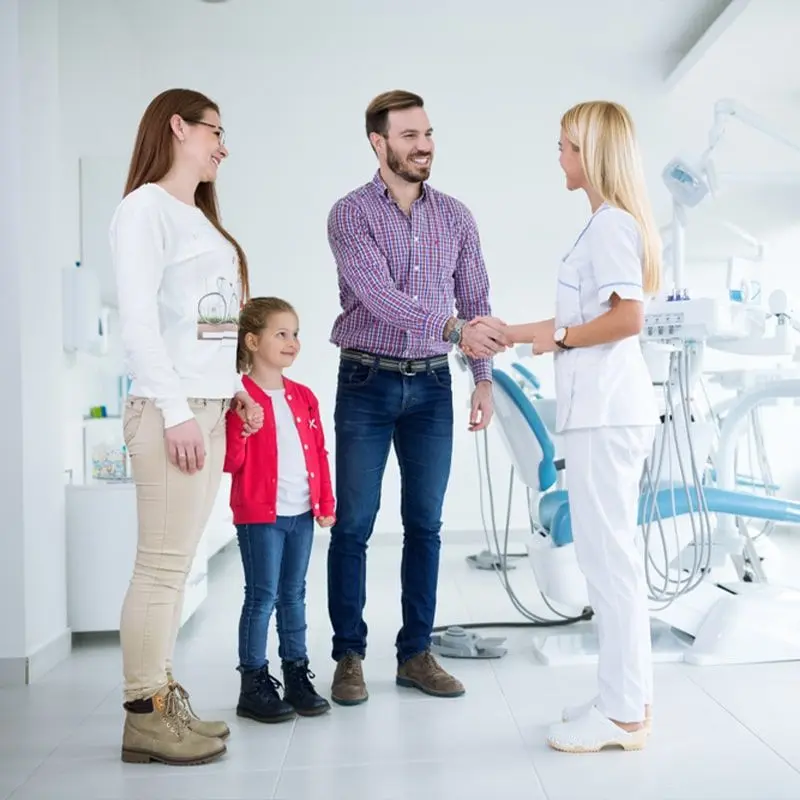 A family of three greets a dentist in a bright dental clinic