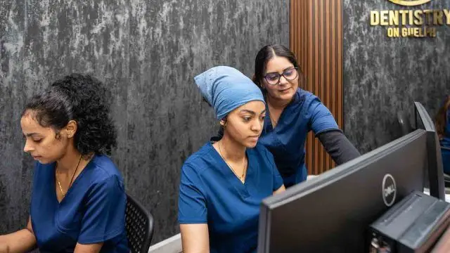 Three team members in navy scrubs work at the computers on the Dentistry on Guelph front desk