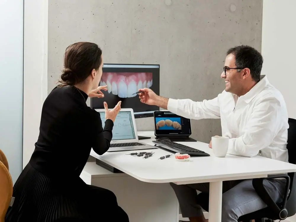 Dentist and patient review digital dental scans on computer screens.