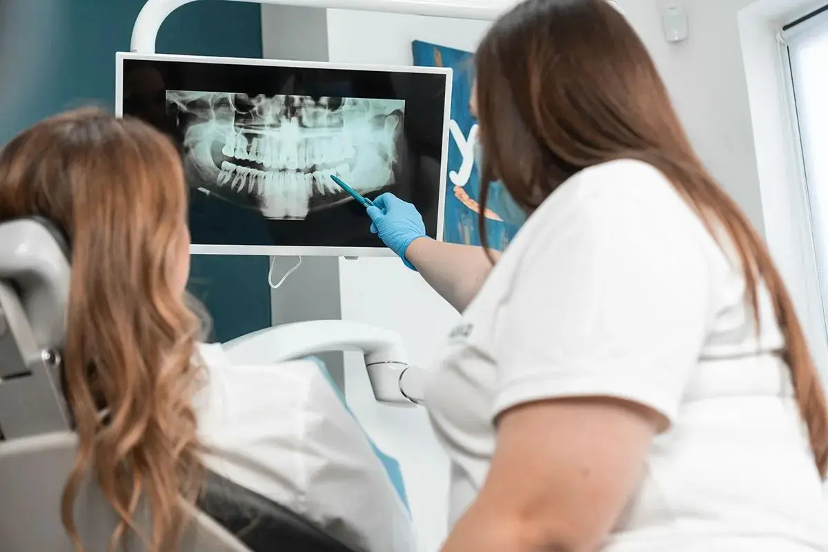 A dental professional shows a patient a panoramic dental X-ray on a screen