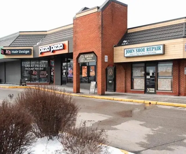 A small shopping plaza with essential services, including Dentistry on Guelph, which offers convenient, personalized dental care. Having a nearby clinic simplifies oral health routines, making regular check-ups easier for early issue detection. The brick and wood-paneled storefronts sit along a wet parking area with patches of snow under an overcast sky.
