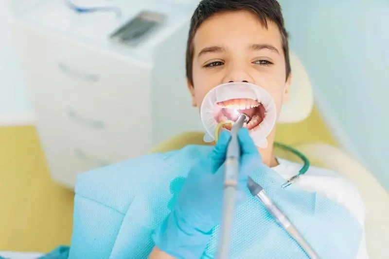 A smiling boy with a cheek retractor during dental treatment