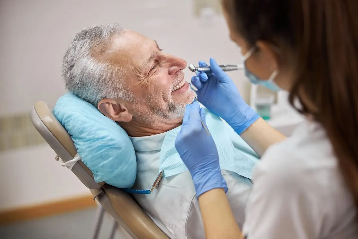 A smiling older man in a dental chair while a dentist in blue gloves works on his teeth