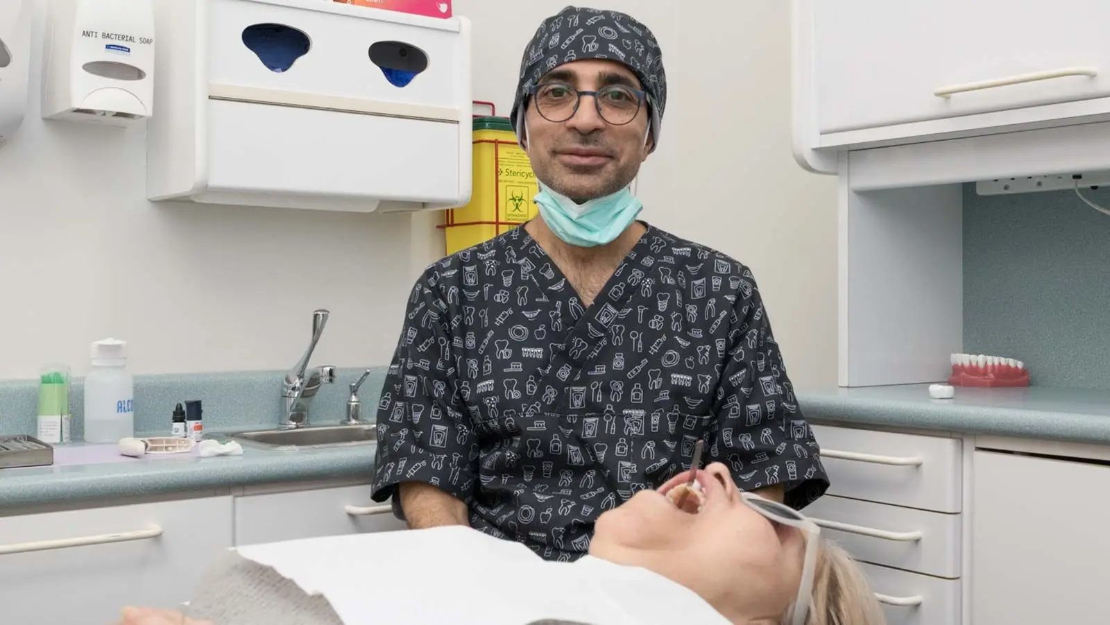 Dr. Reza Shahhaidari in scrubs and cap looks at patient in dental chair.