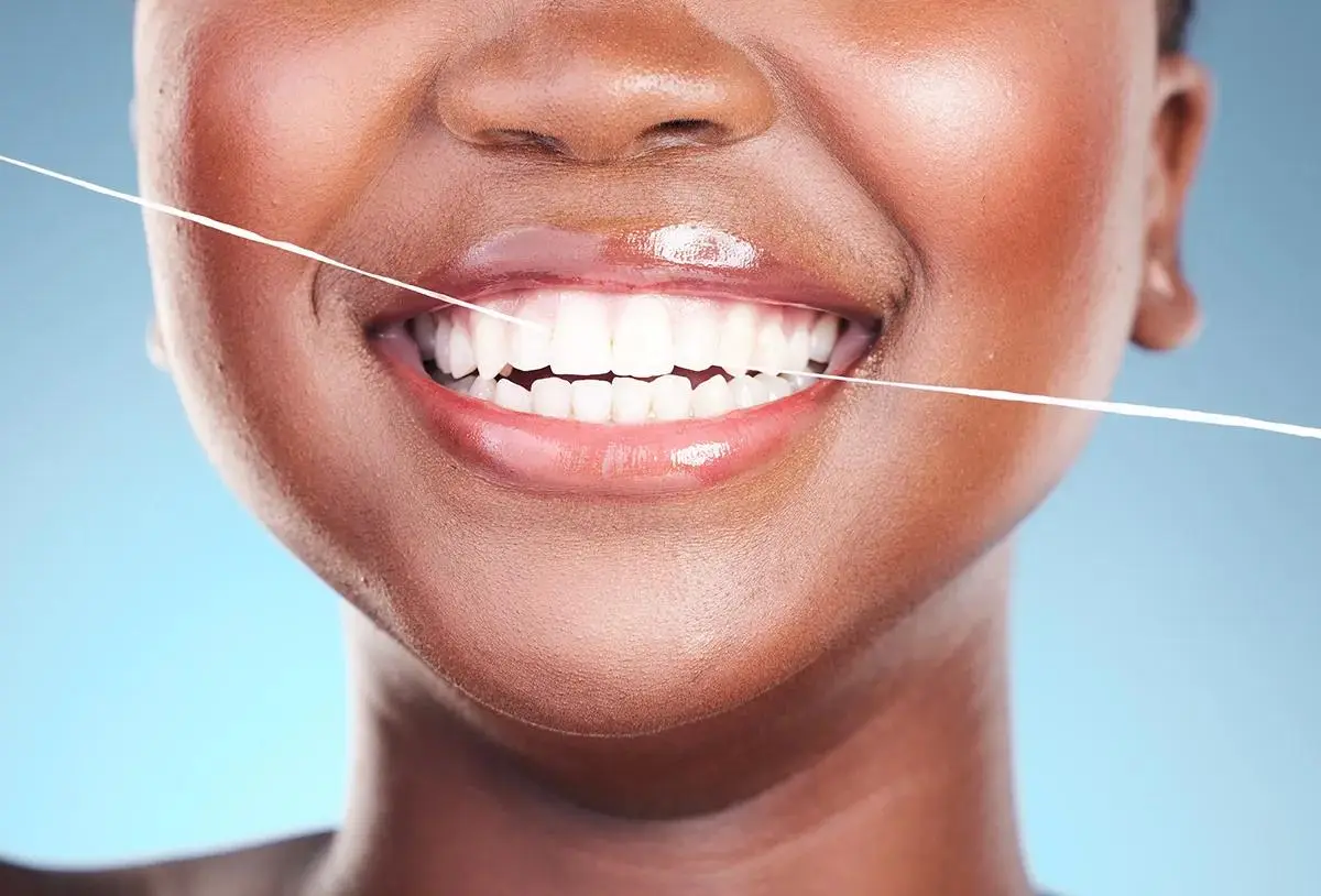 Closeup of person flossing their bright white teeth against blue background, highlighting the importance of proper dental flossing technique