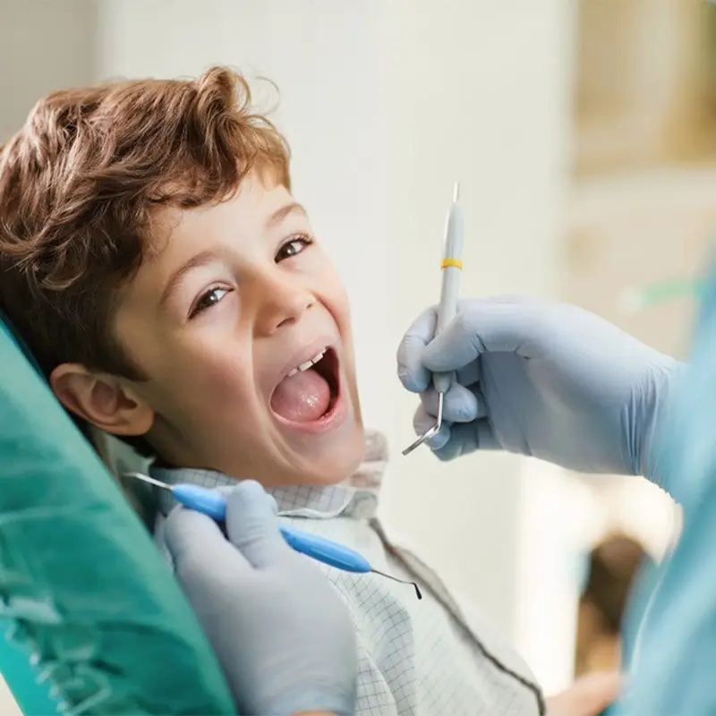 A laughing boy in a dental chair while a gloved hand holds a dental instrument