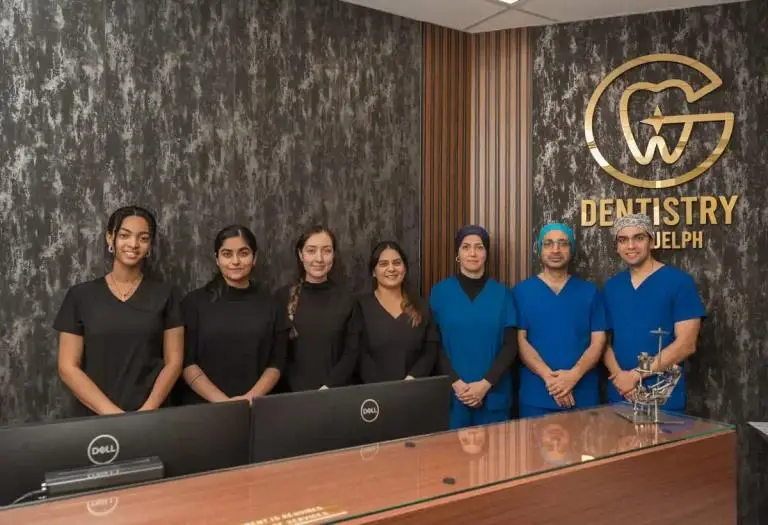 The Dentistry on Guelph team standing at the reception desk under the gold clinic logo