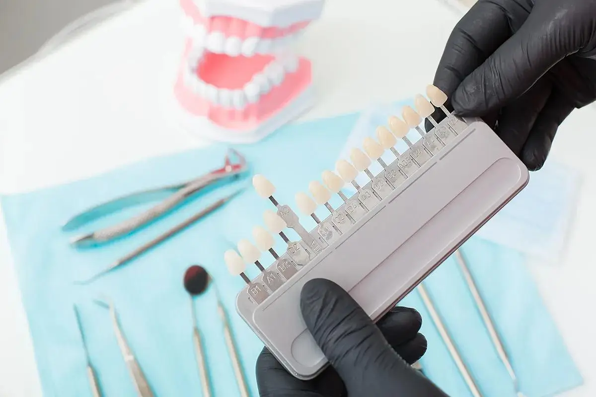 Dental instruments, a model of teeth and a tooth shade guide held by gloved hands