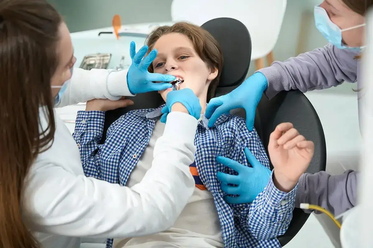 Child receiving dental treatment from two dental professionals, showcasing pediatric dentistry and collaborative care approach