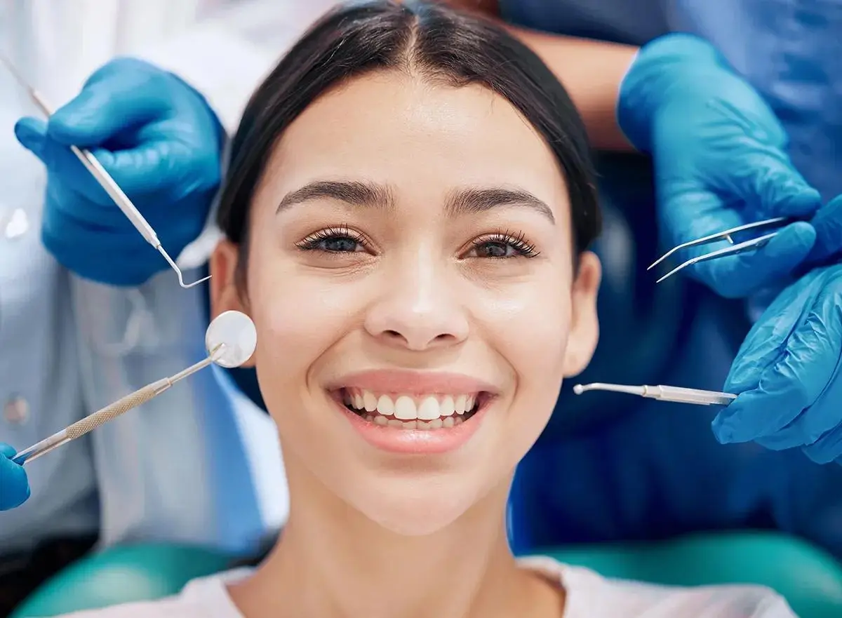 Smiling dental patient during examination with multiple dental instruments positioned around teeth, showcasing modern dental examination procedures.
