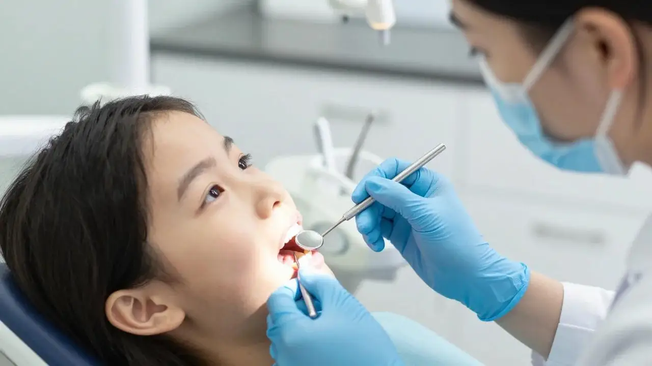 A dentist checks a young girl's teeth with a small mirror