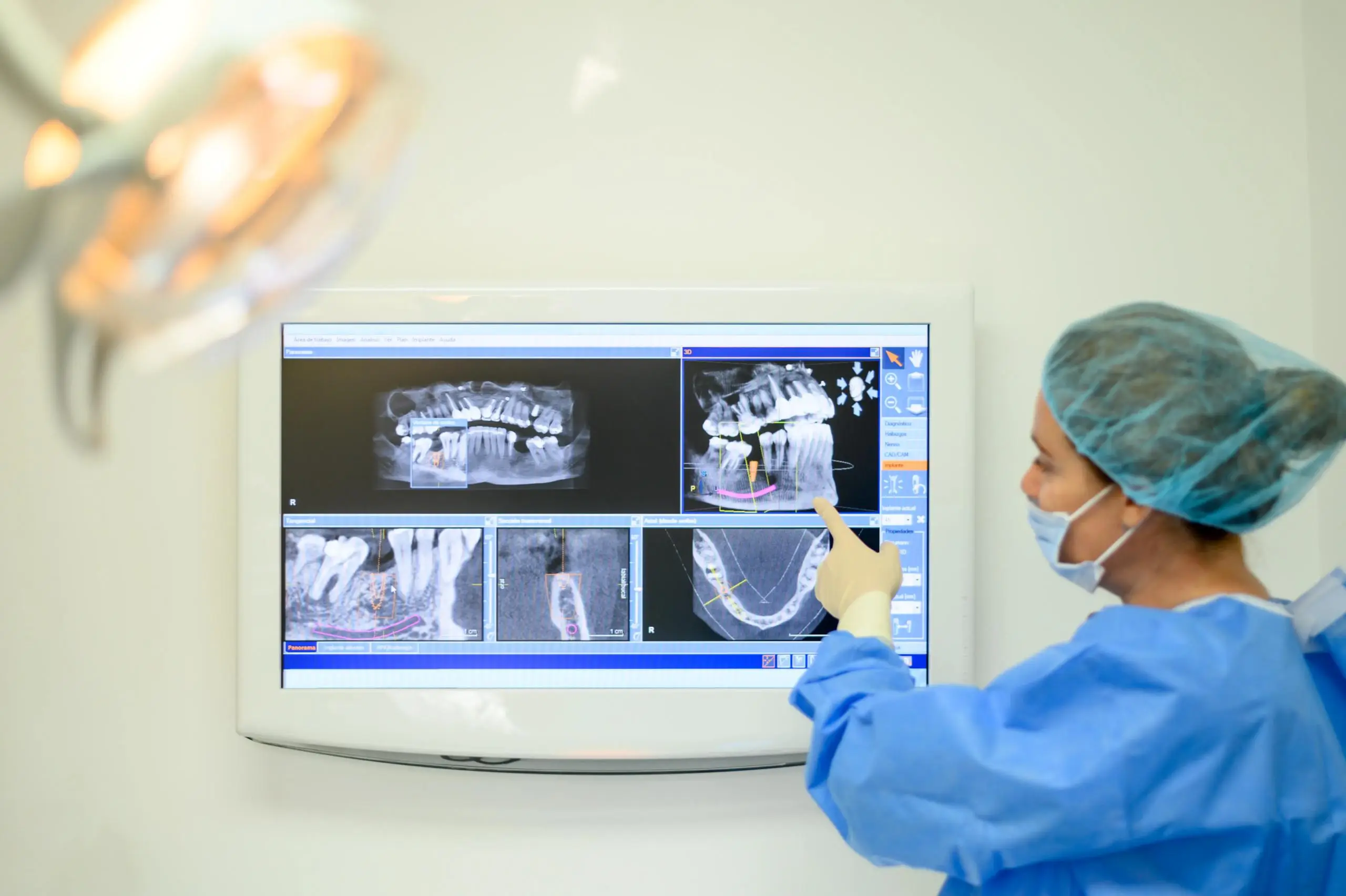 A dental professional points to dental X-ray images on a wall-mounted screen