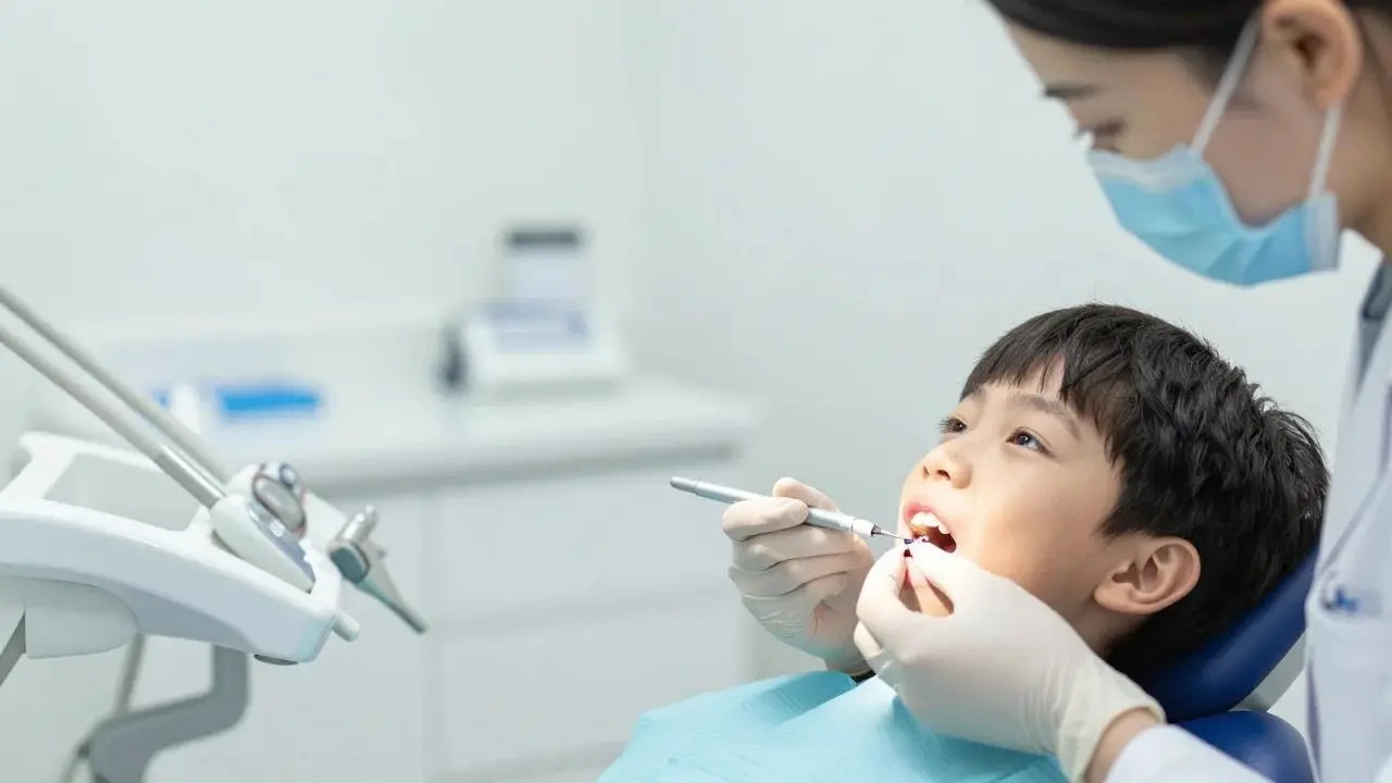 A dentist treats a boy's teeth as he sits in a dental chair