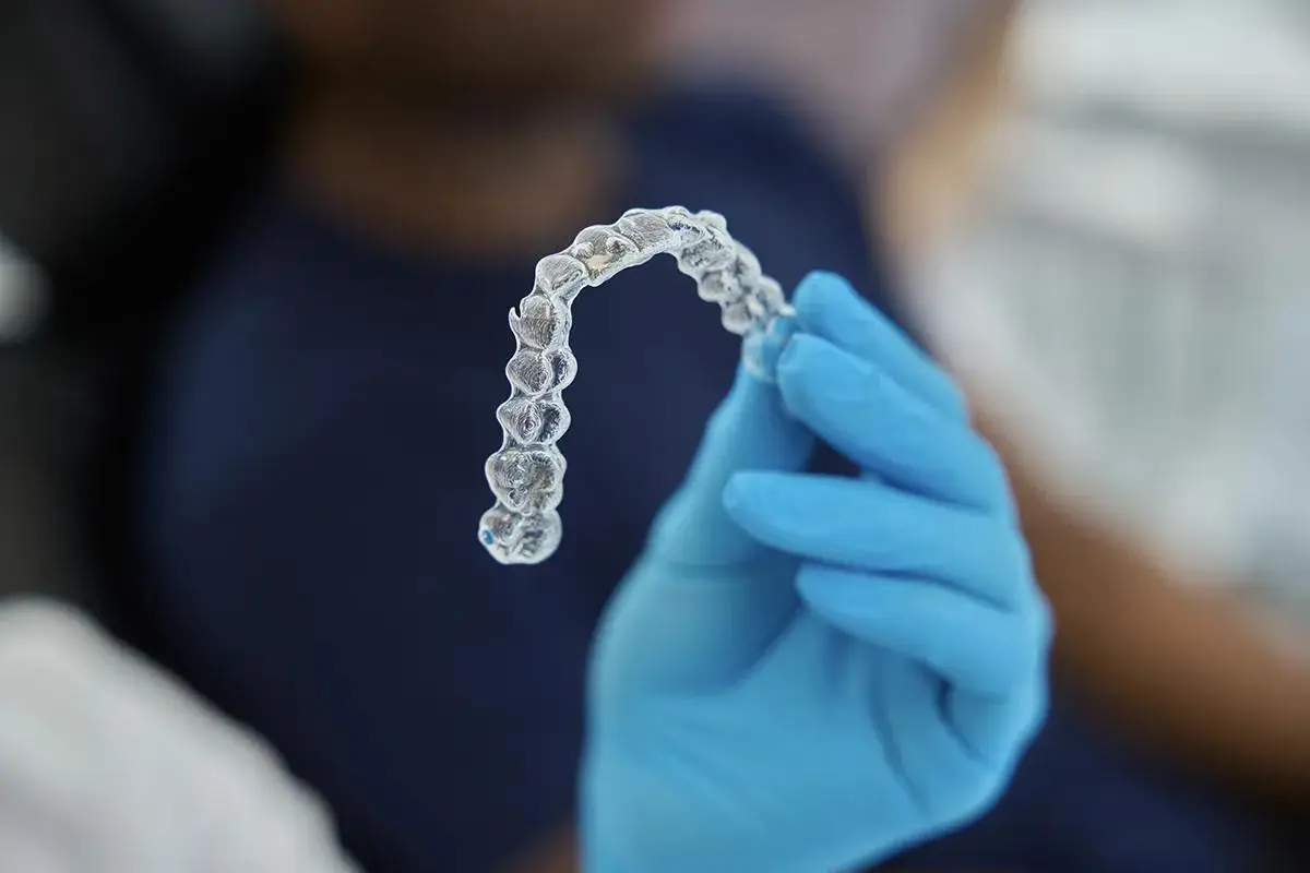A clear Invisalign aligner tray being held by a dental professional wearing blue gloves