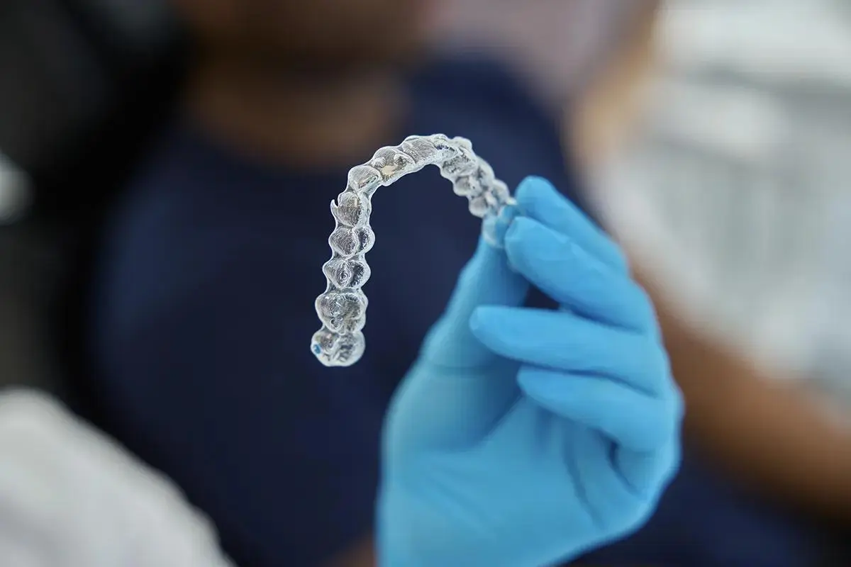 A clear Invisalign aligner tray being held by a dental professional wearing blue gloves