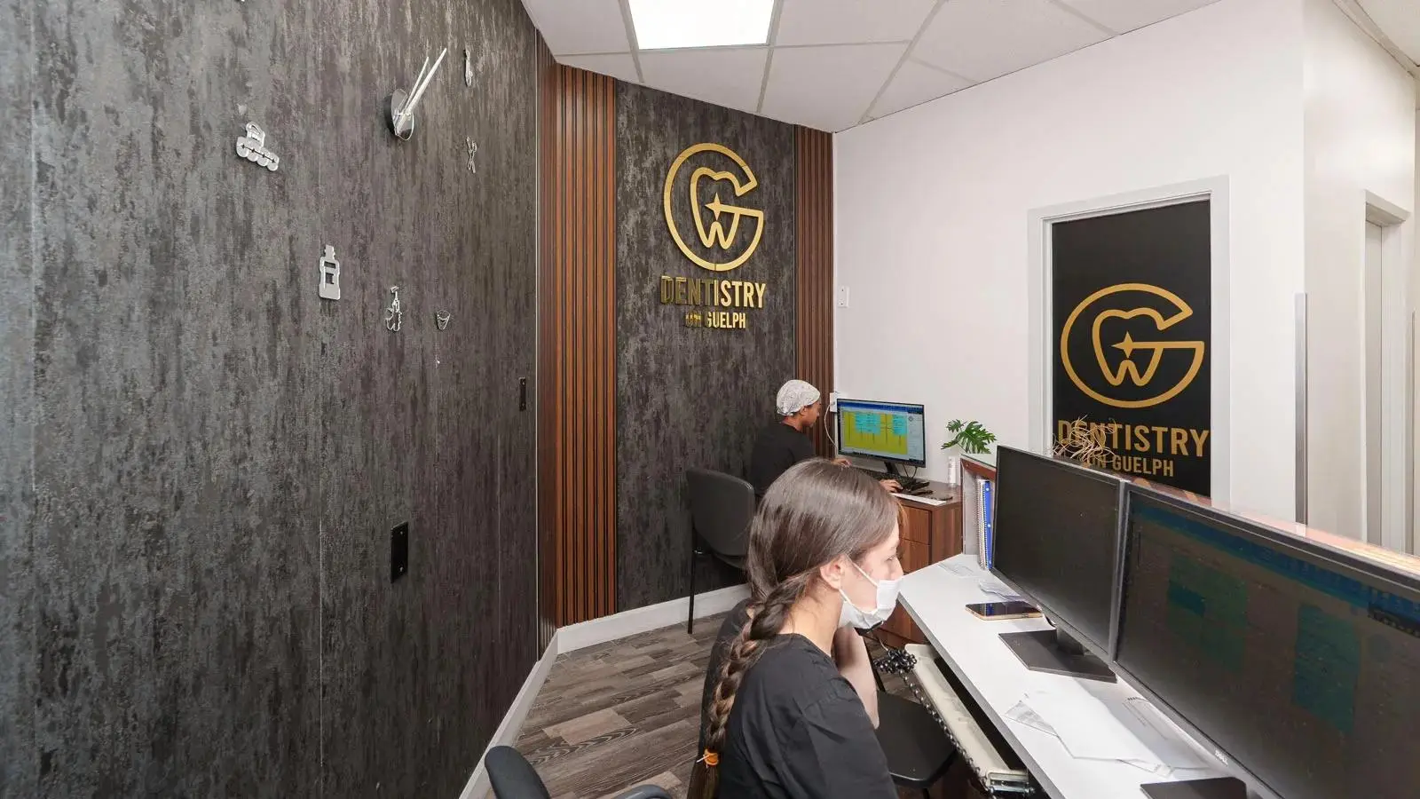 Dentistry on Guelph clinic reception with staff at computers and "Dentistry on Guelph" logo.