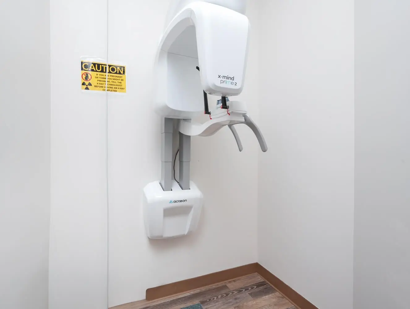 X-Mind Prime 2 panoramic dental X-ray machine installed in a clean, modern dental clinic. The unit is mounted on the wall and features advanced imaging technology for precise and comprehensive dental diagnostics. A caution sign is displayed nearby, ensuring patient safety during X-ray procedures.