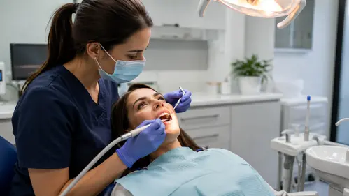 A dentist in a mask treats a reclining patient's teeth